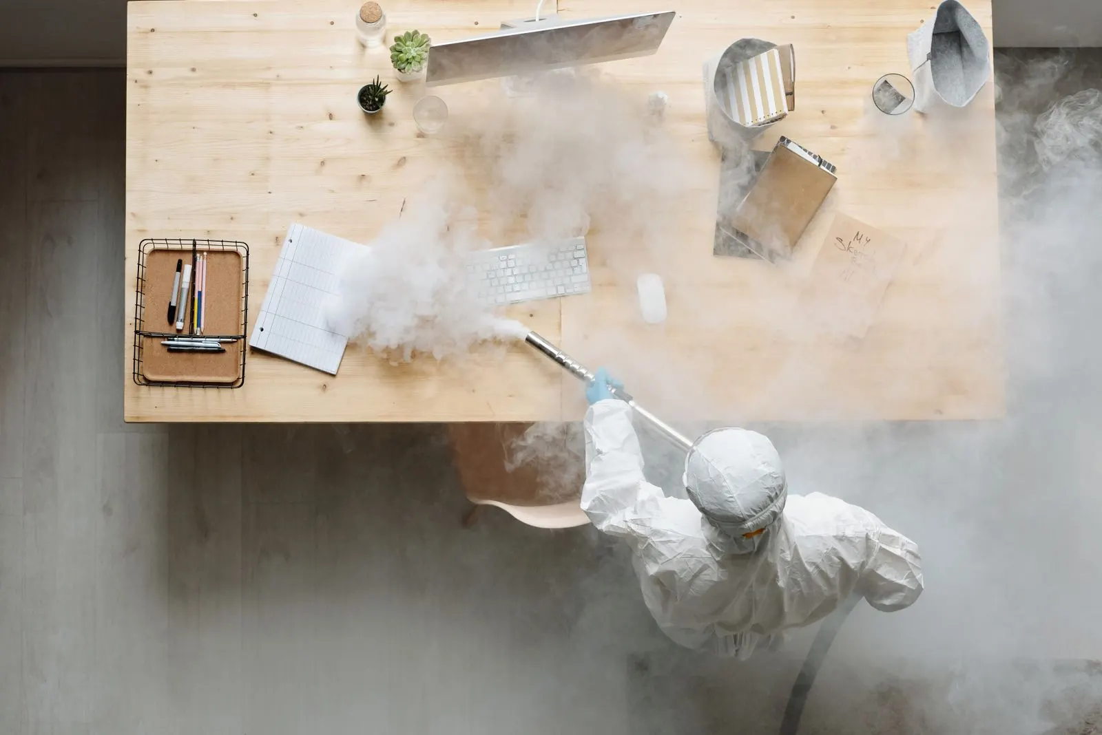 Worker in protective gear sanitizing an office from above