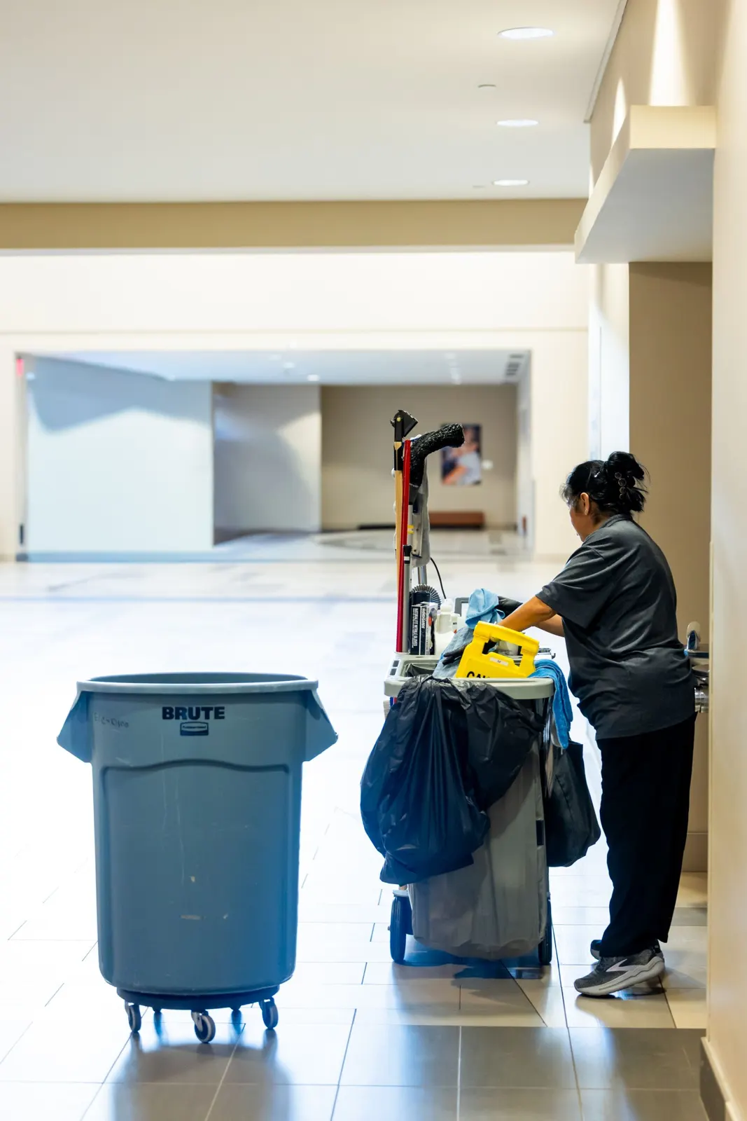 Janitor pushing a cleaning cart down a bright hallway