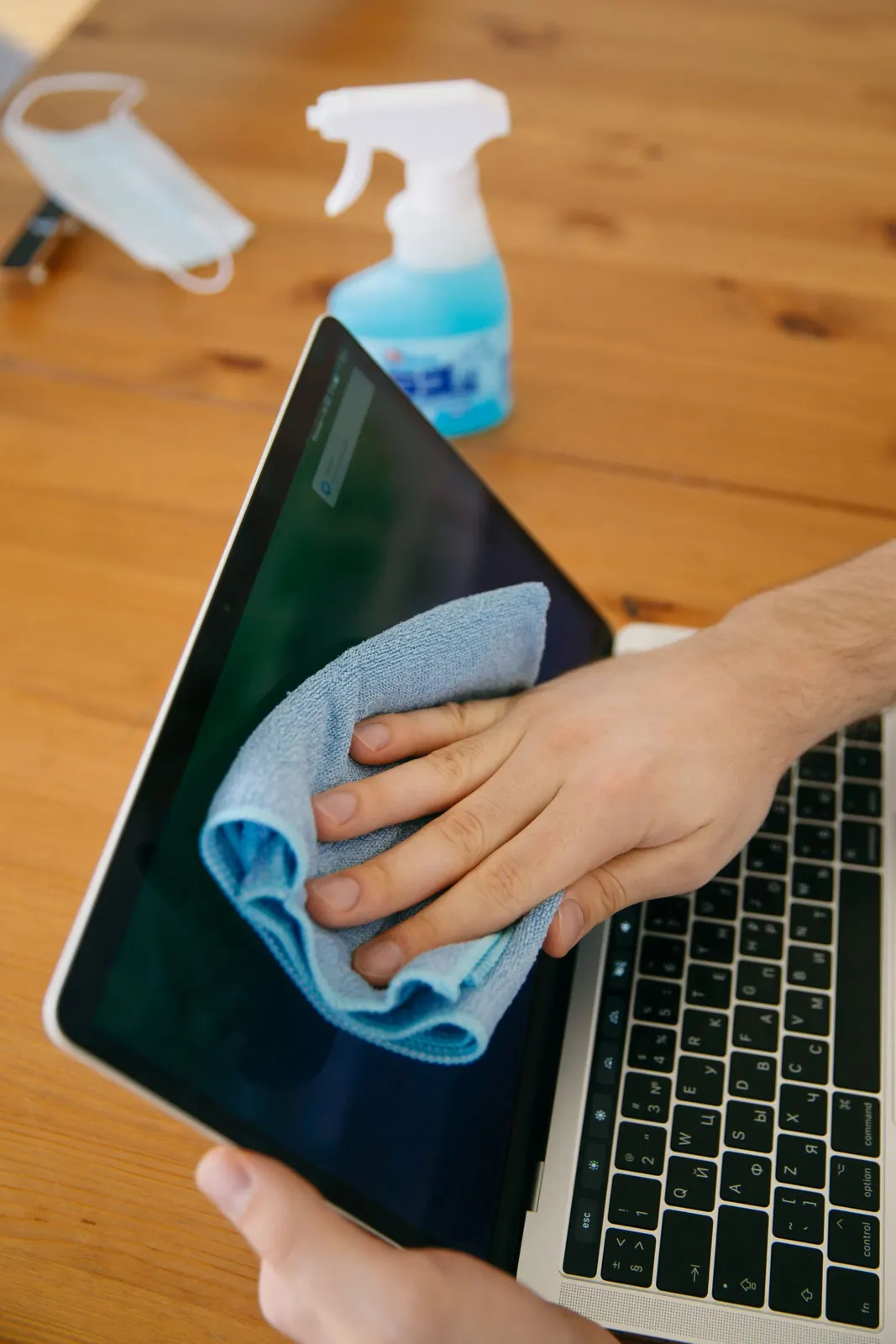 Hand wiping a laptop screen with a microfiber cloth and spray