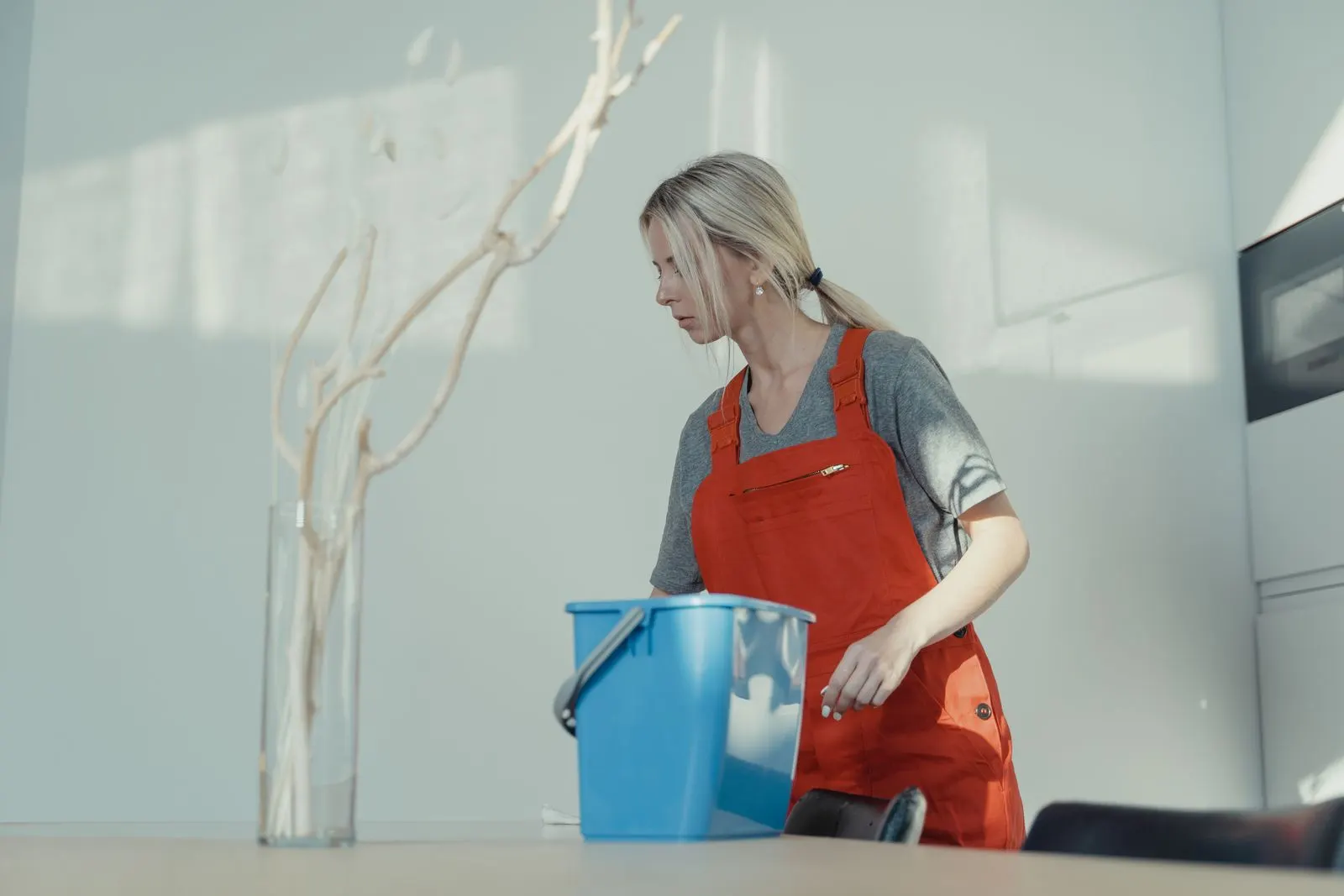Cleaner in uniform wiping a counter with a bucket and cleaning supplies nearby