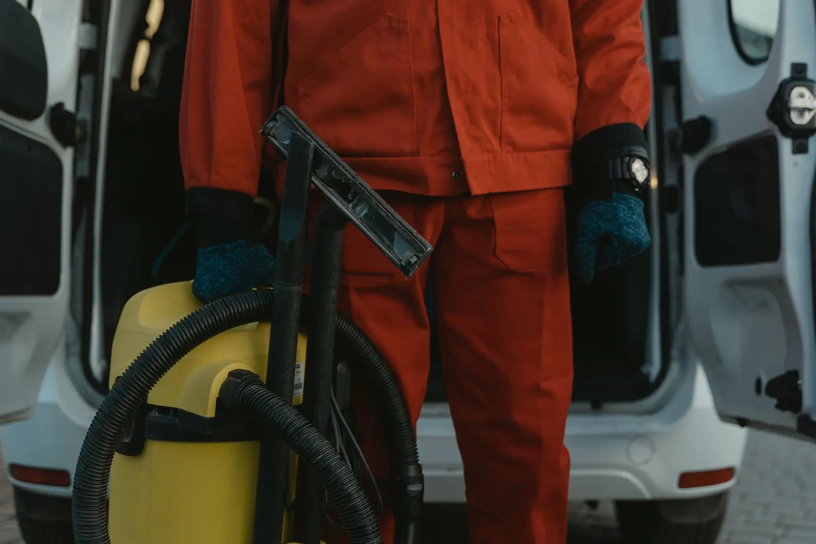 Cleaner in uniform with a commercial vacuum beside a service van